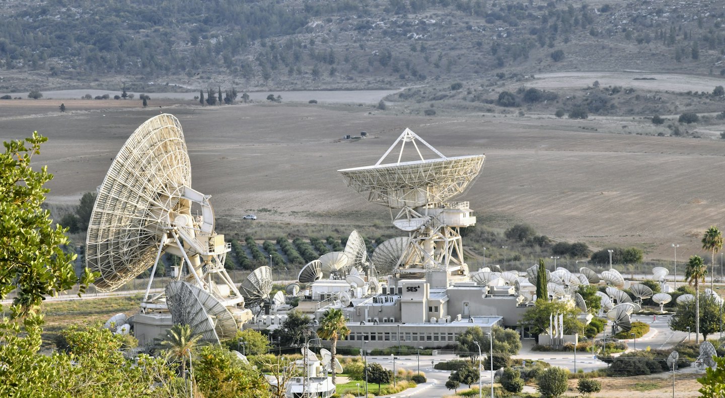 Satellite ground station with large dishes in arid landscape.